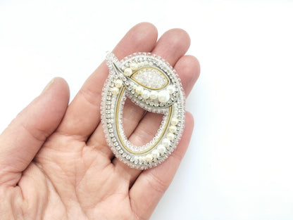 A hand holding a decorative piece of jewelry, which appears to be a brooch or pendant.