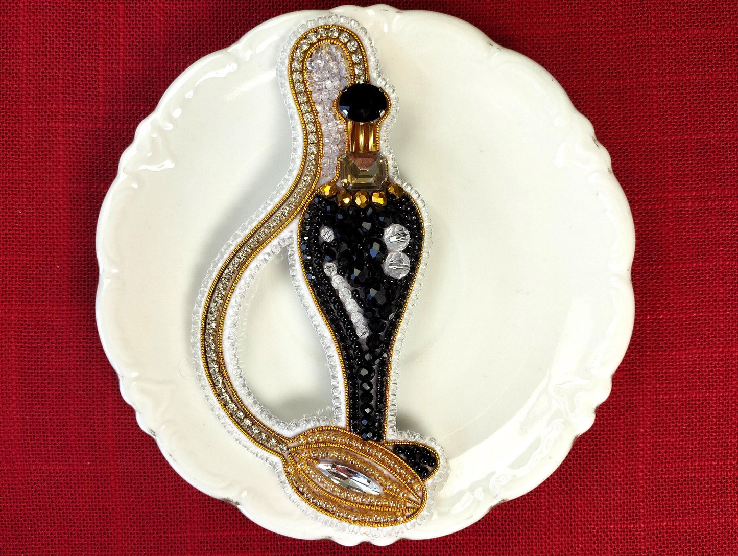 A decorative black perfume bottle with gold accents and rhinestones is displayed on a white plate against a red background.