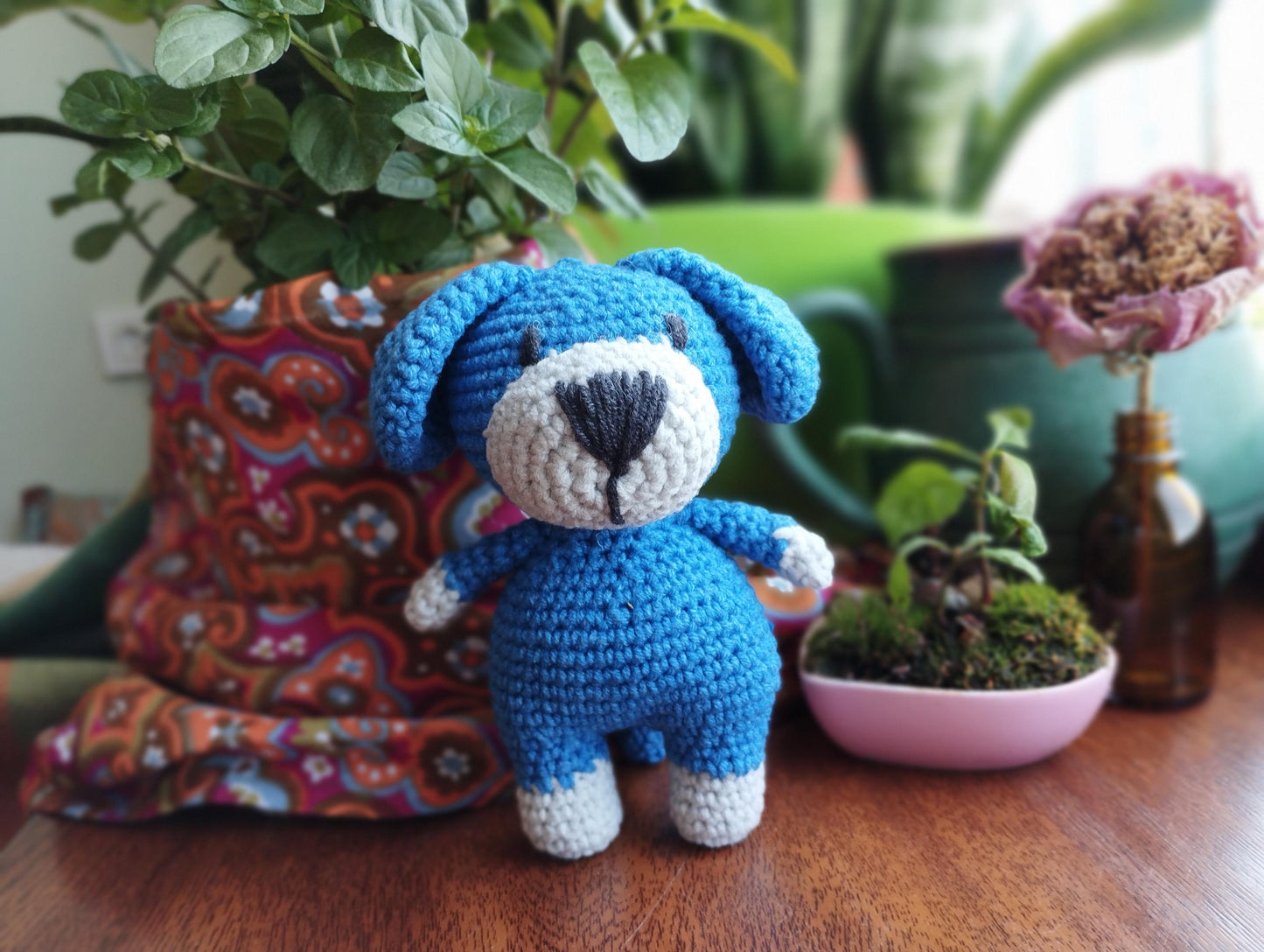 a crocheted blue teddy bear sitting next to a potted plant