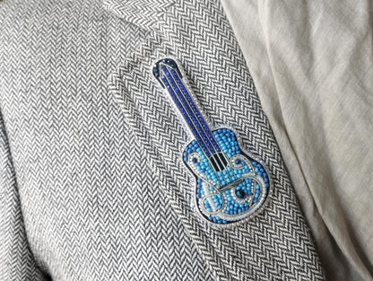 A close-up of a person's jacket lapel, showing a decorative blue and silver guitar-shaped pin or badge.