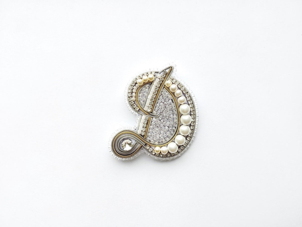 A decorative piece made of various materials, including pearls, beads, and metal, is displayed against a white background.