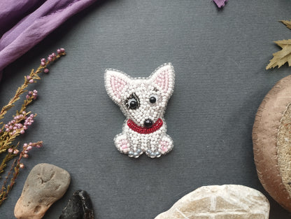 a small, intricately crafted embroidered dog brooch, surrounded by various natural elements such as rocks, leaves, and flowers.