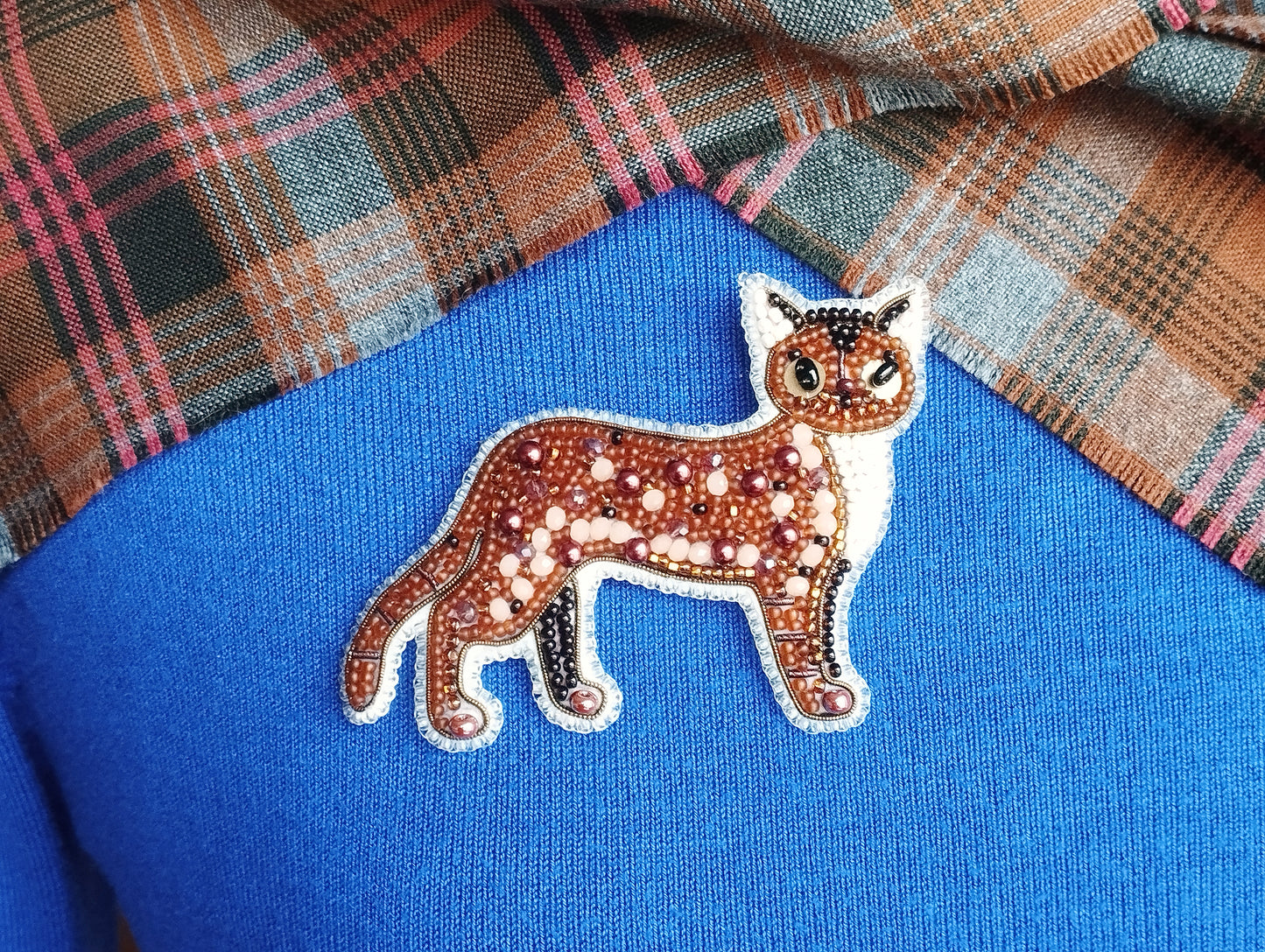 A close-up image of a beaded cat pin on a blue fabric background.