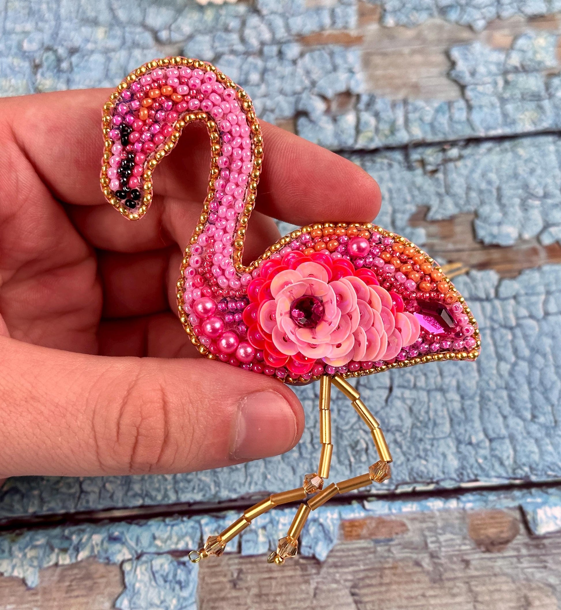 a hand holding a pink flamingo brooch