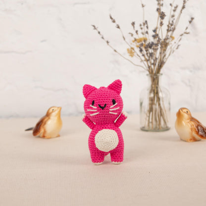 a pink crocheted cat standing next to three small birds