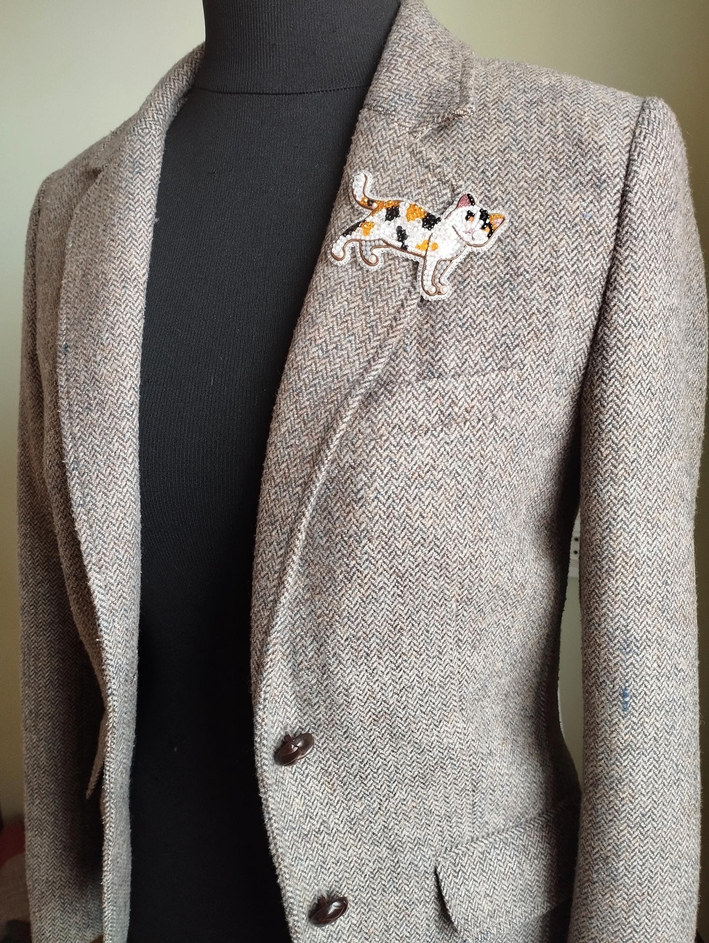 A gray tweed jacket with a black turtleneck sweater underneath, and a decorative cat embroidered patch on the left breast area.
