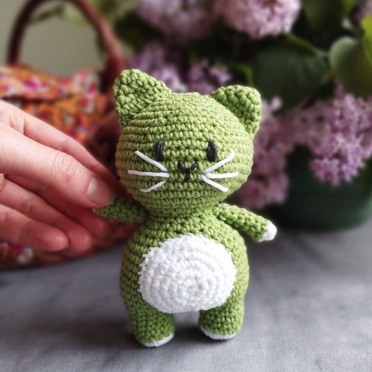 a green cat sitting on top of a table next to a pair of scissors