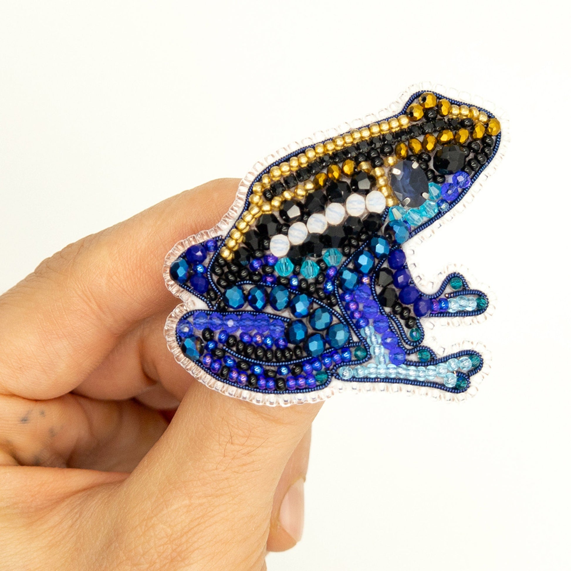 a hand holding a blue and yellow frog brooch