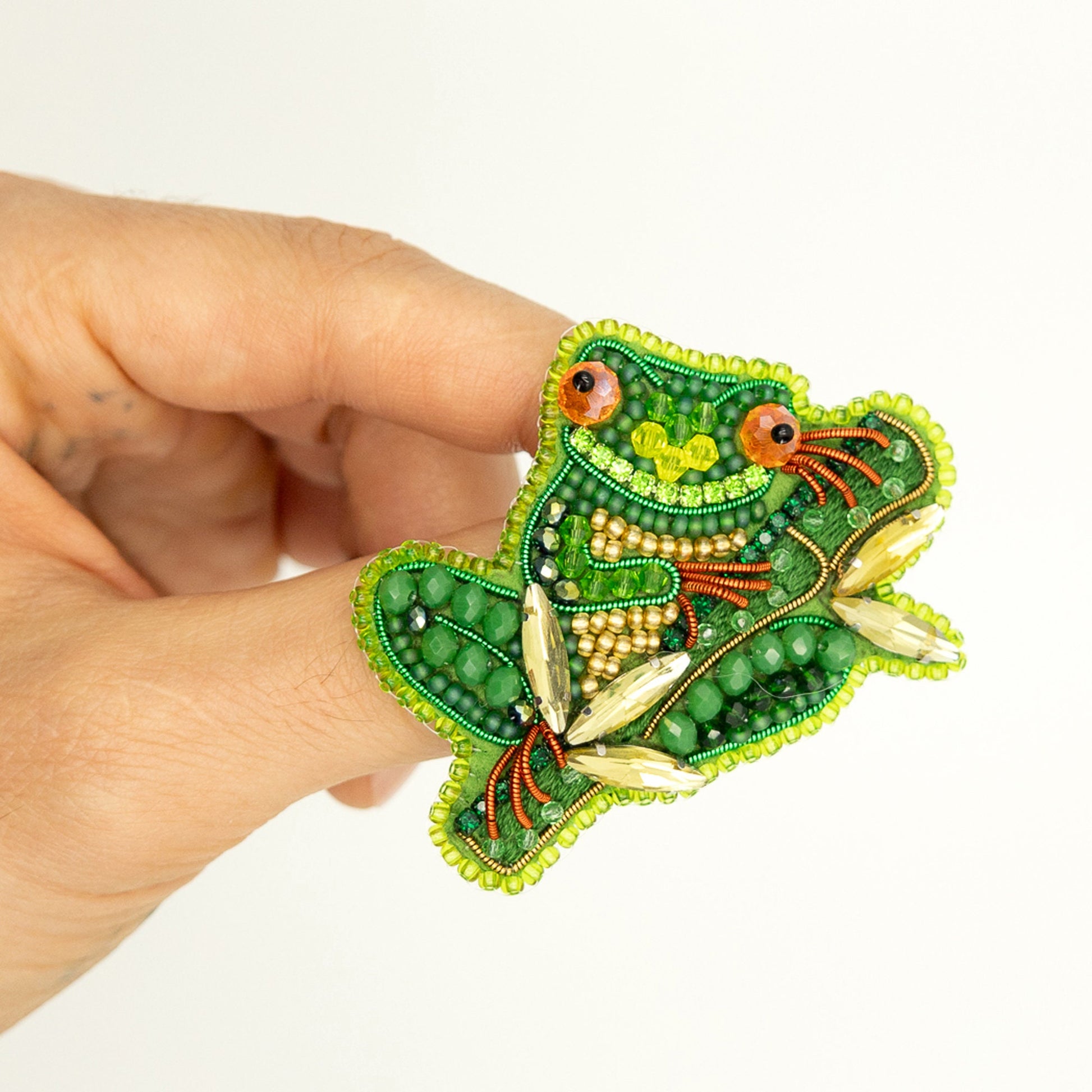 a person is holding a green frog brooch