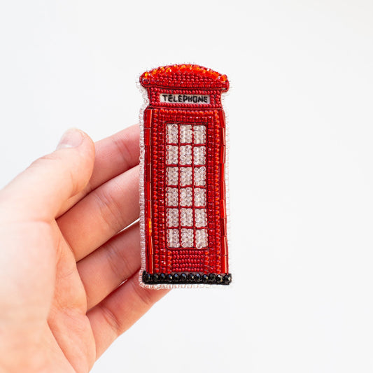 a hand holding a small red phone booth