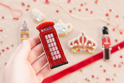 a hand is holding a beaded red phone booth