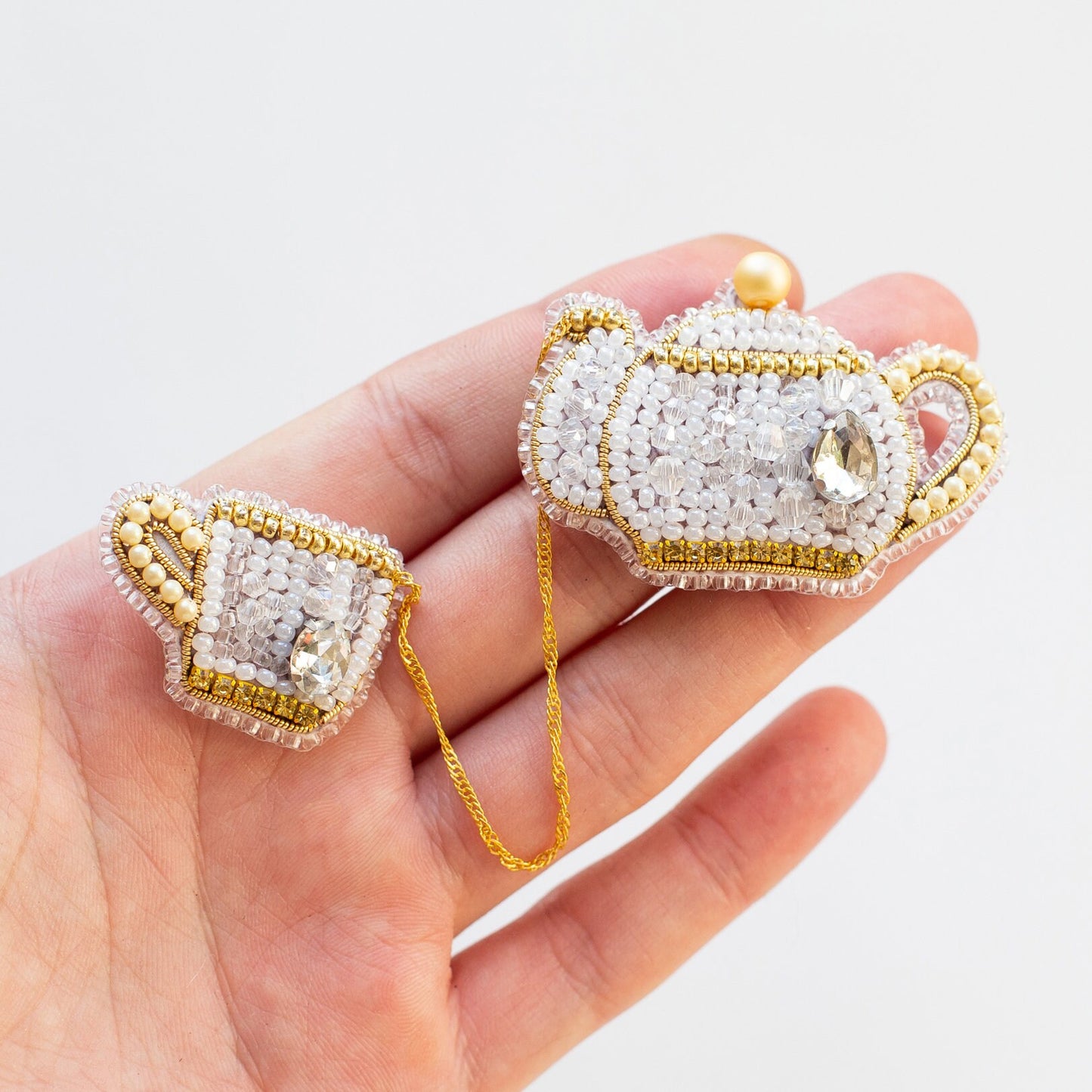 a hand holding two small white and gold brooches