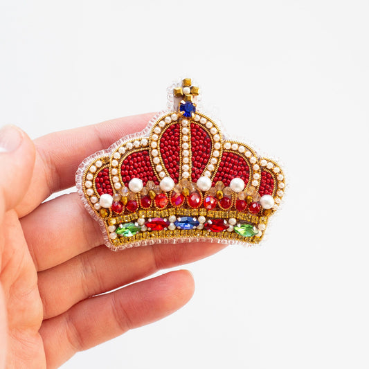 a hand holding a red and gold crown brooch