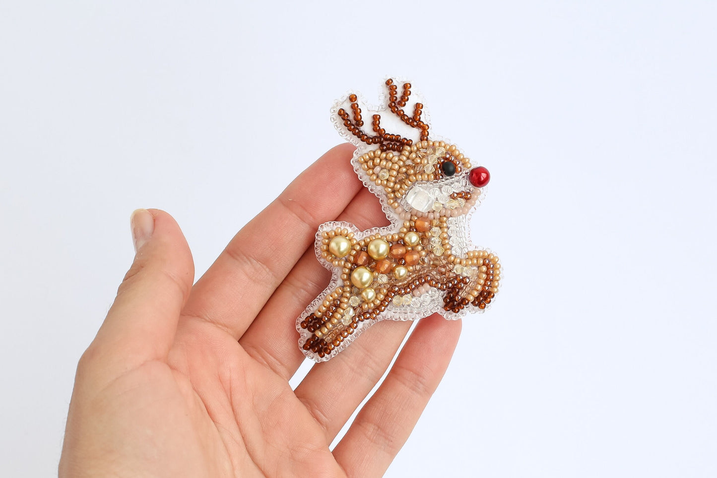 a hand holding a small beaded reindeer ornament