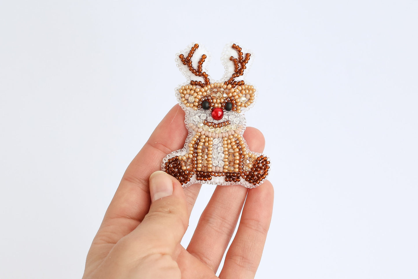 a hand holding a beaded reindeer ornament