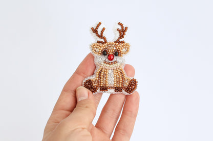 a hand holding a beaded reindeer ornament