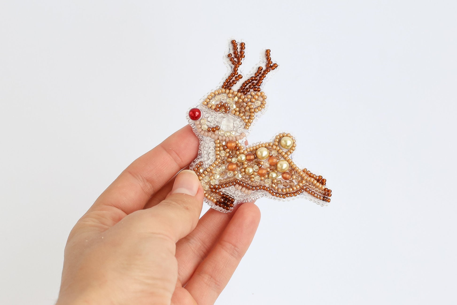 a hand is holding a beaded reindeer ornament