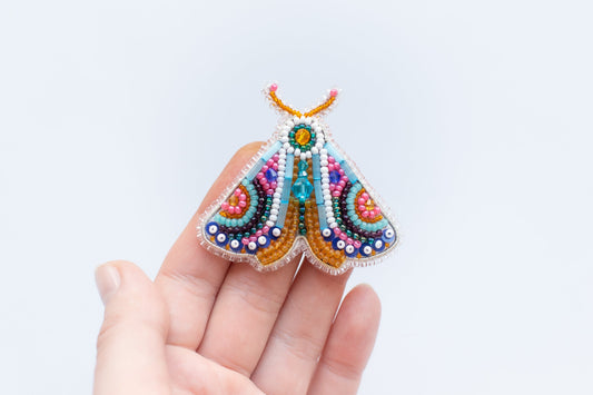 a hand holding a colorful beaded butterfly brooch