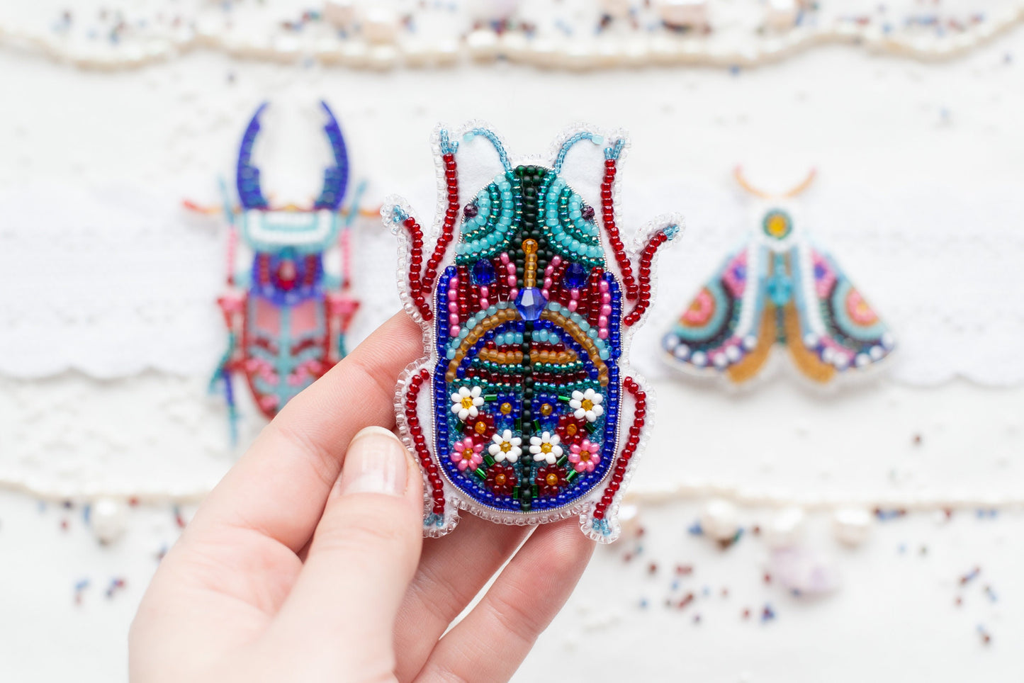 a hand holding a beaded bug next to a pair of earrings