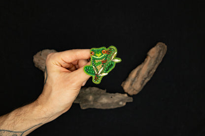 a hand holding a green brooch with a red flower