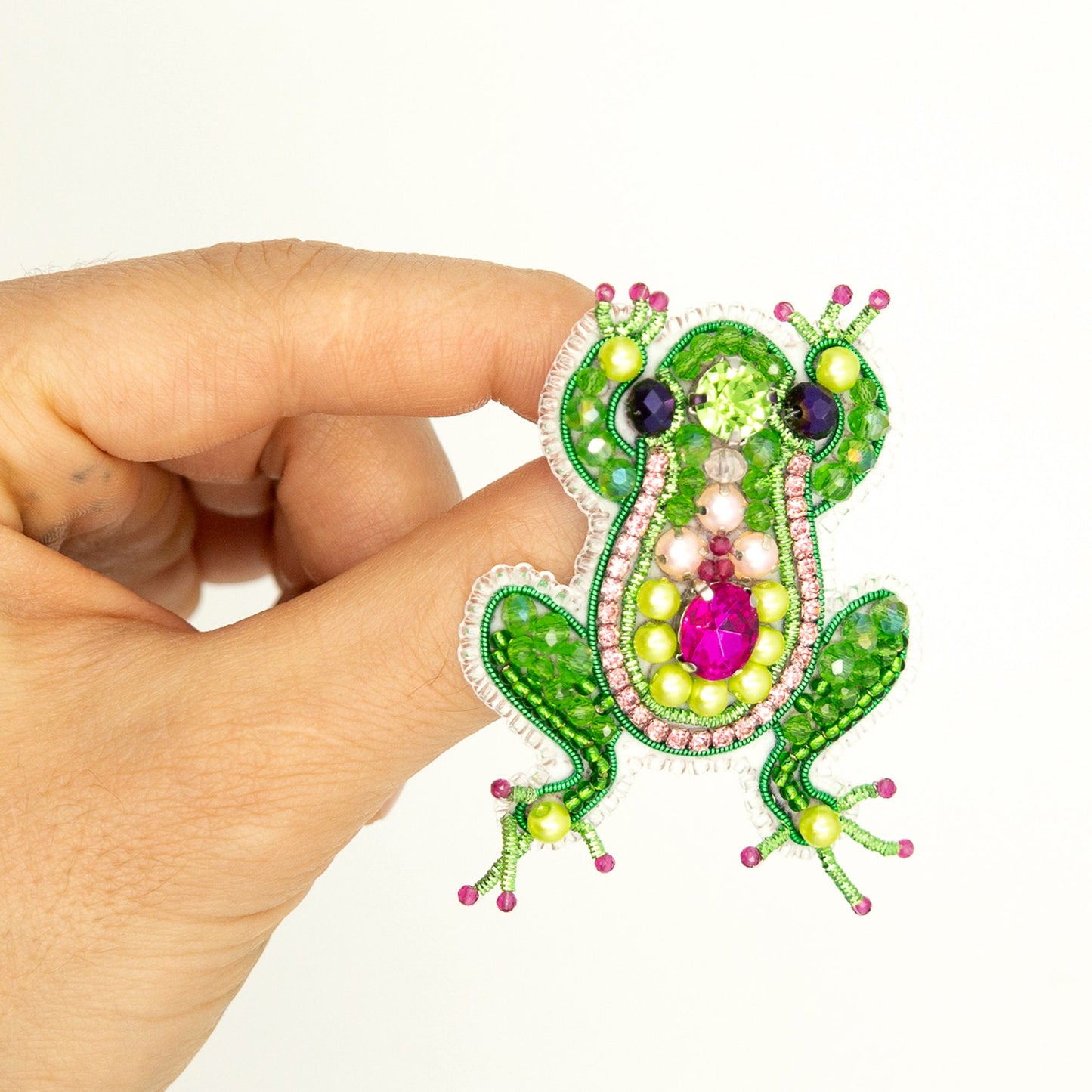 a hand holding a green and pink frog brooch