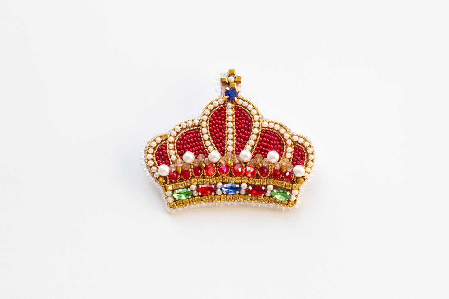 a red and gold crown brooch sitting on top of a white surface