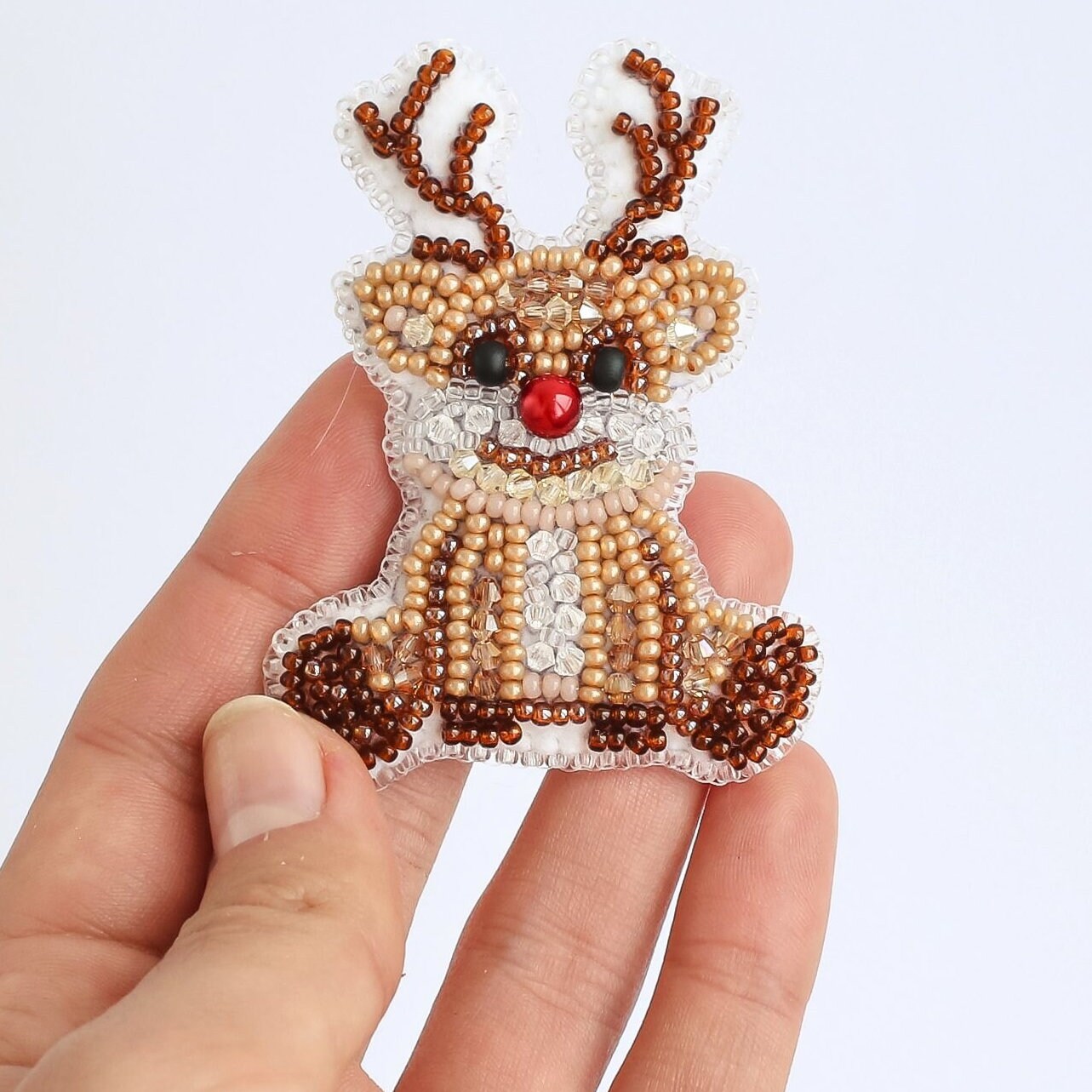 a hand holding a small beaded reindeer ornament