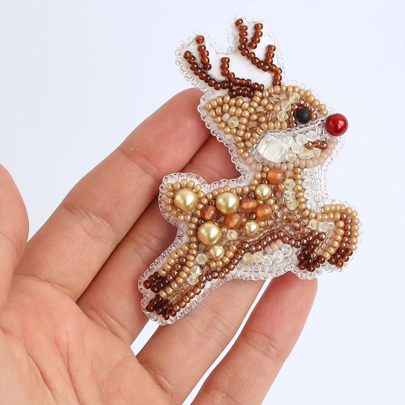 a hand holding a small beaded reindeer ornament