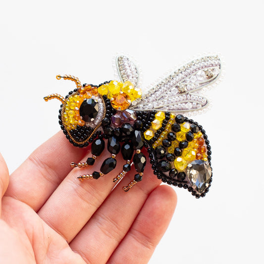 a hand holding a beaded bee on a white background