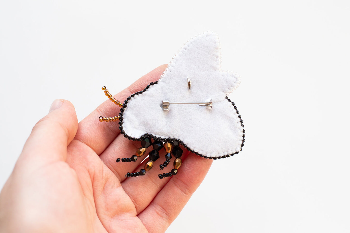 a hand holding a tiny white brooch with black beads