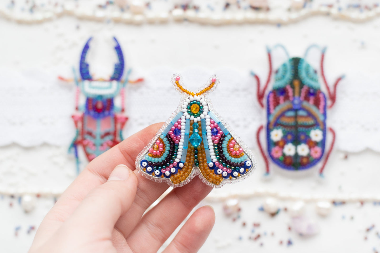 a hand holding a beaded insect in front of a pair of shoes