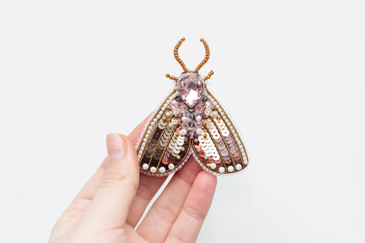 a hand holding a brooch with a bug on it