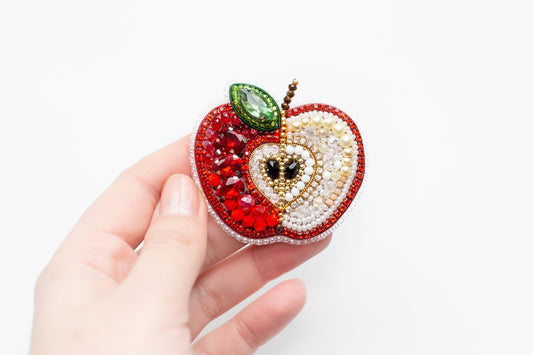 a hand holding an apple shaped brooch