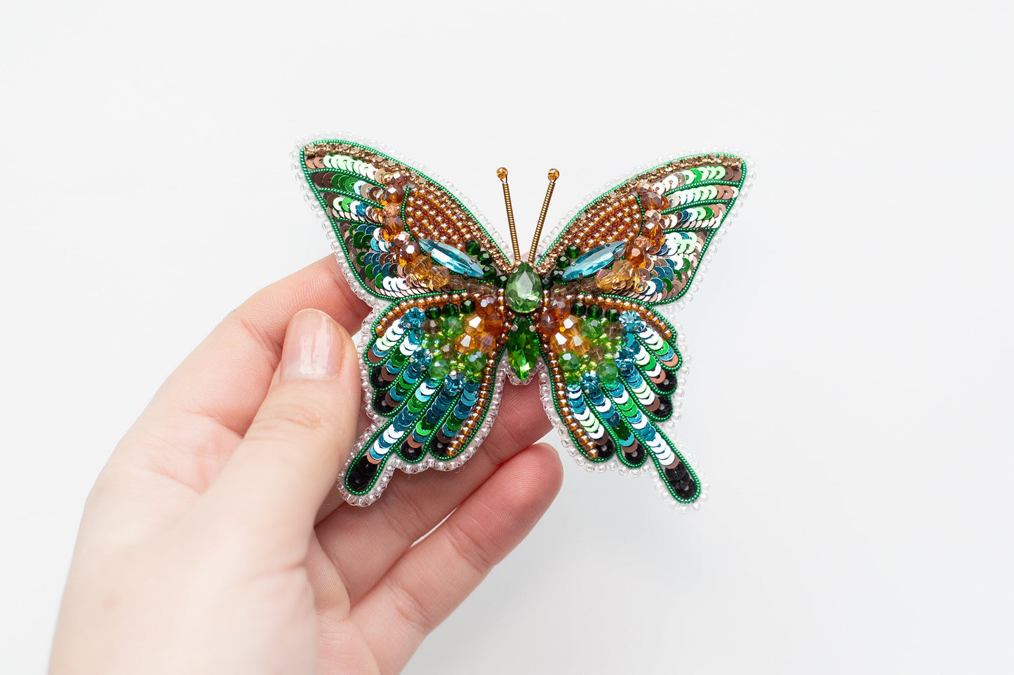 a hand holding a colorful butterfly brooch