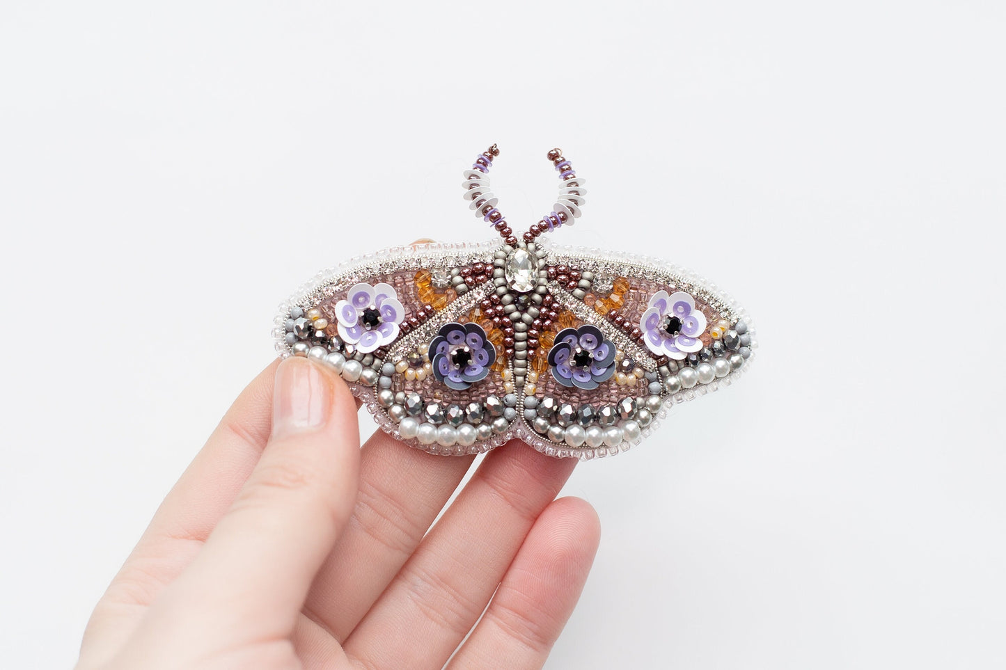 a hand holding a beaded butterfly brooch