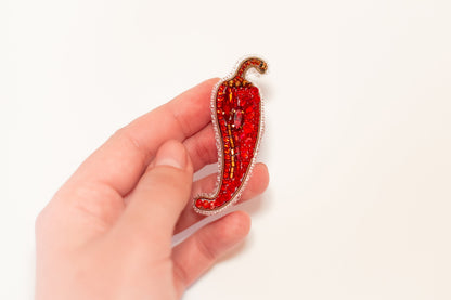 a person is holding a brooch with a red chili on it