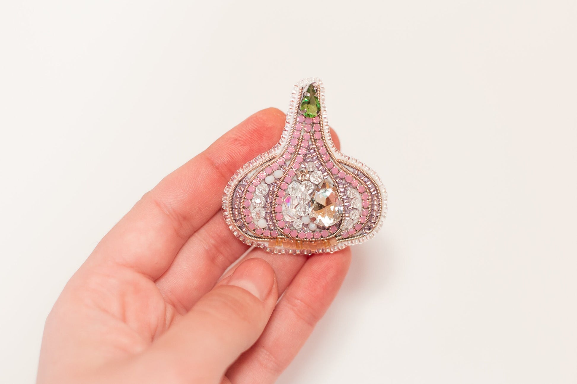 a hand holding a pink and green brooch