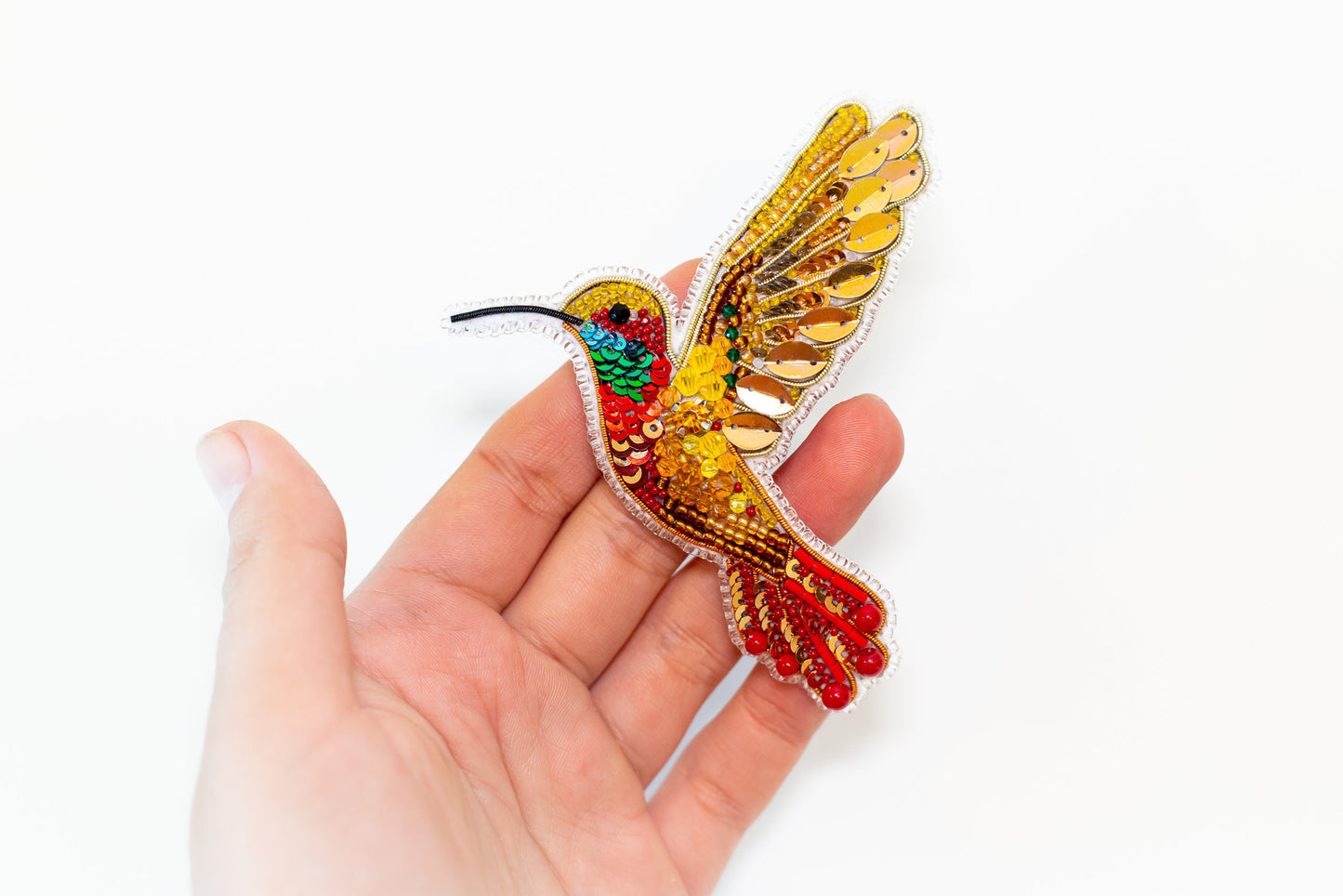 a hand holding a small colorful bird brooch