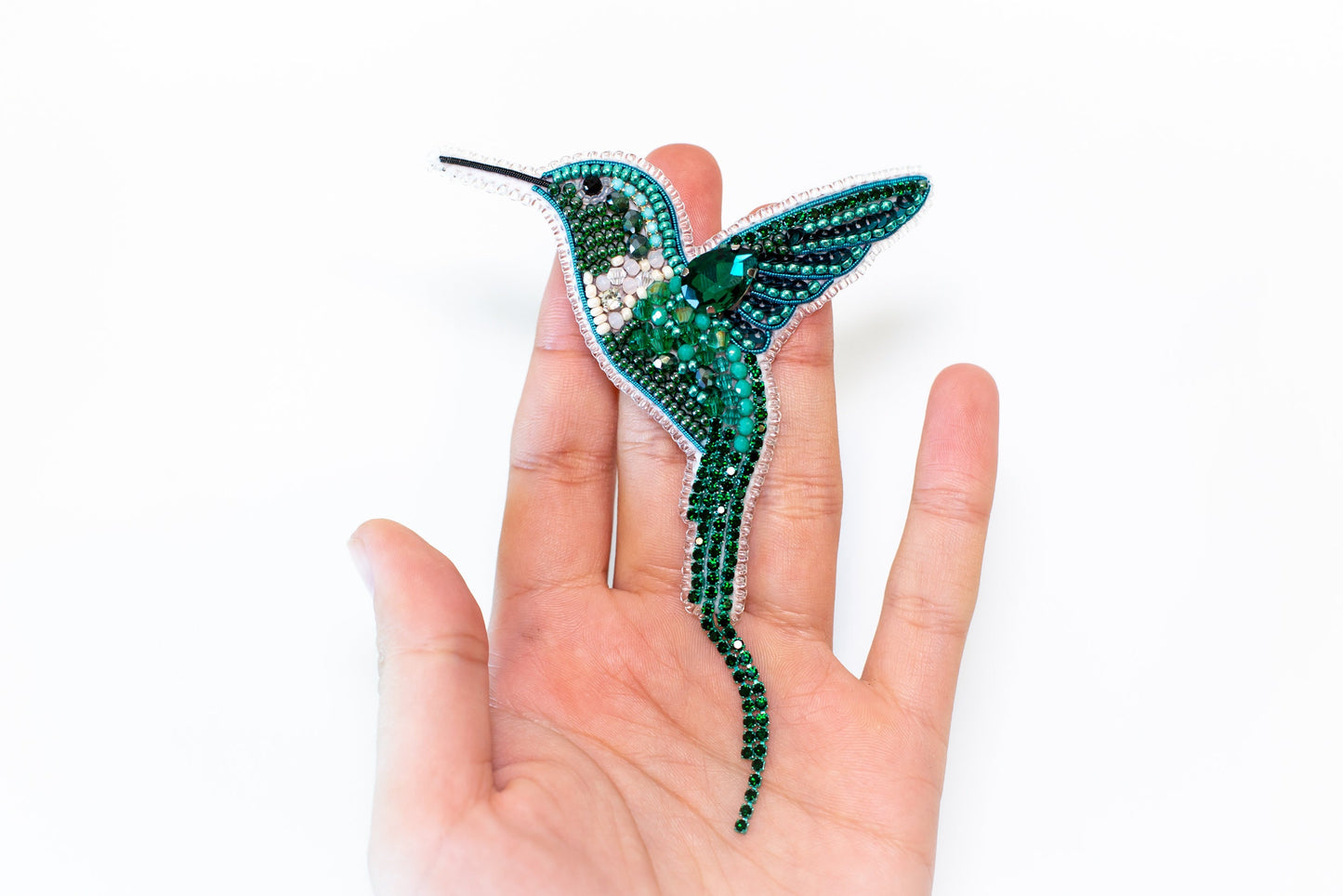 a hand holding a green beaded hummingbird brooch