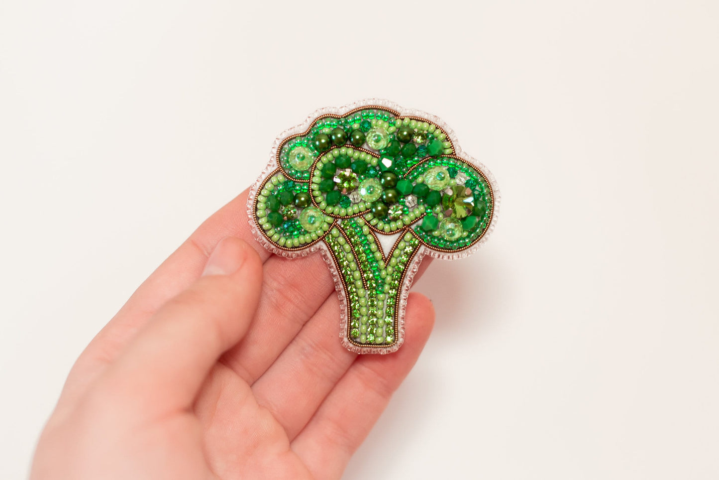 a hand holding a broccoli brooch in it&#39;s palm