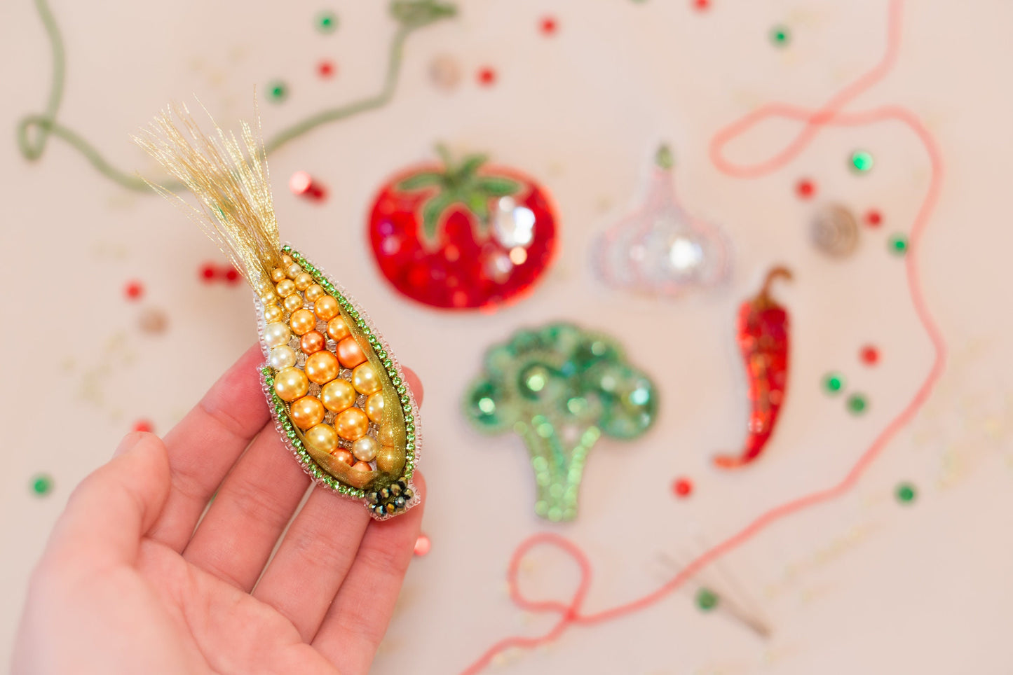 a hand holding a beaded corn on the cob ornament