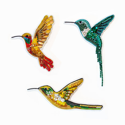 a hand holding a green beaded hummingbird brooch