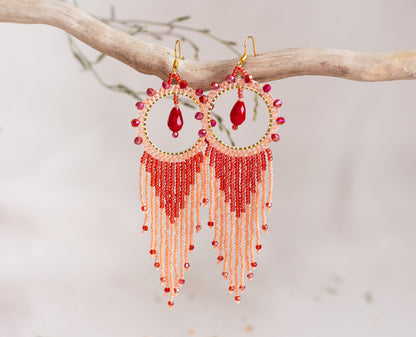 a pair of red beaded earrings hanging from a tree branch