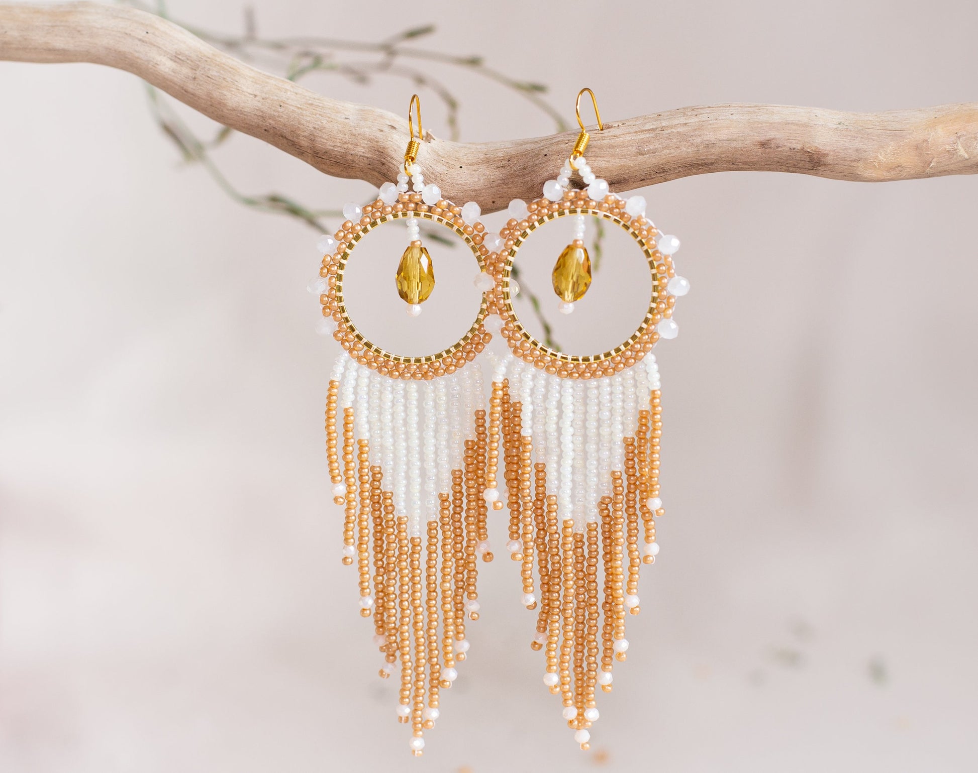 a pair of gold and white beaded earrings hanging from a branch