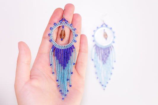 a pair of blue beaded earrings hanging from a tree branch