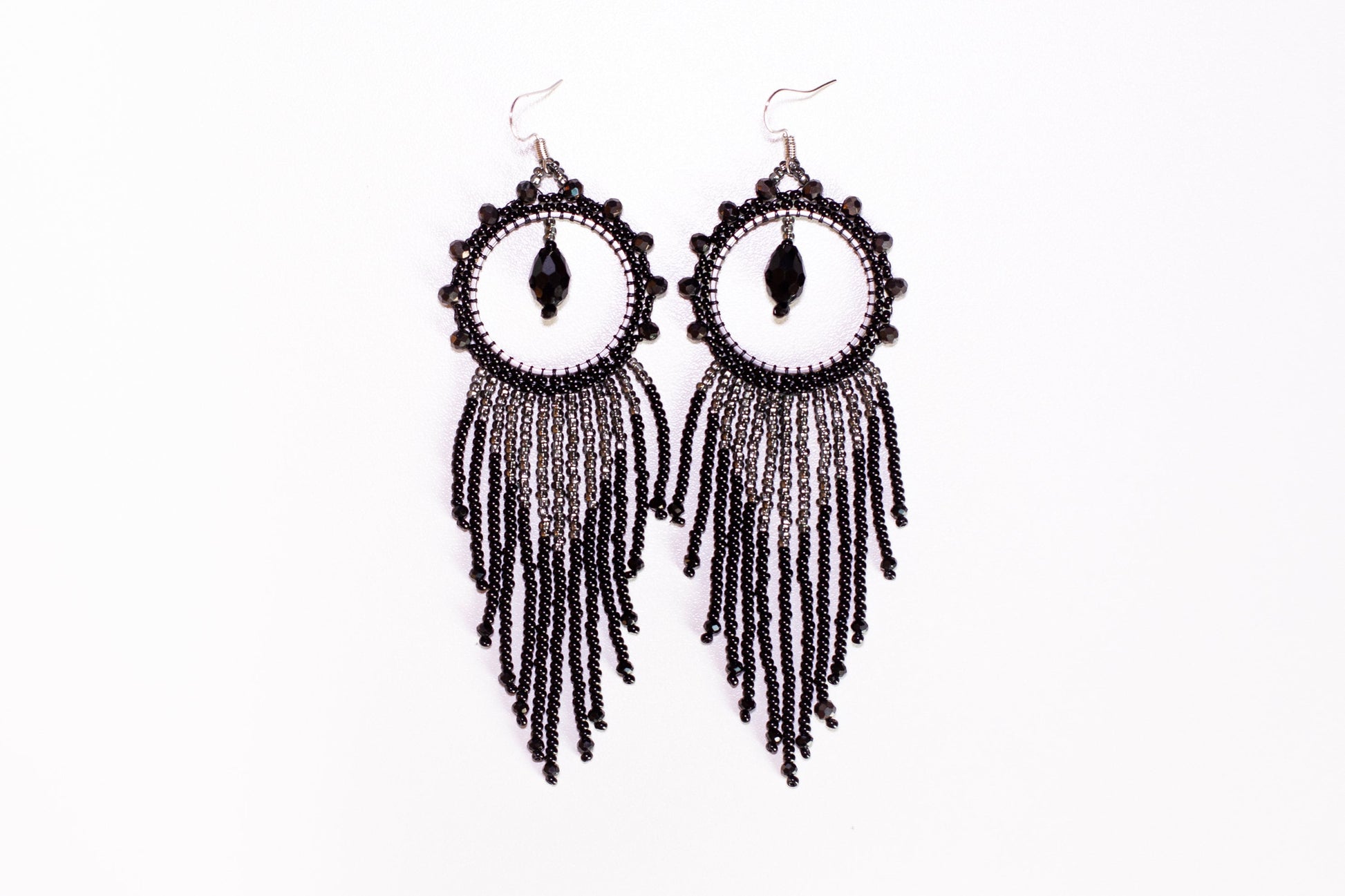 a pair of black beaded earrings hanging from a branch