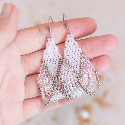 a pair of white beaded earrings on a pink background