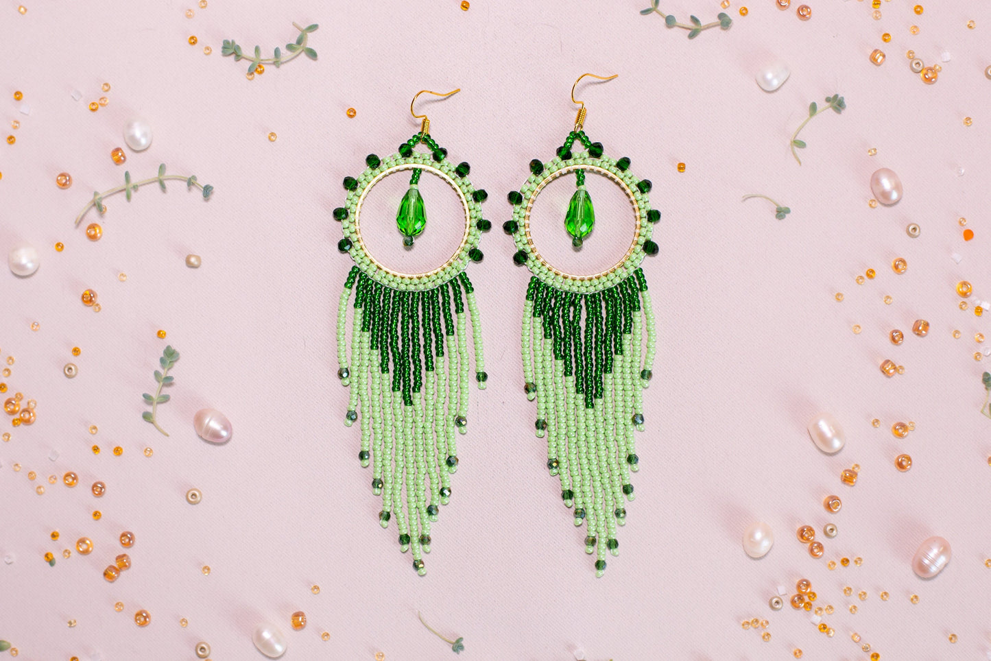 a pair of green beaded earrings on a pink background