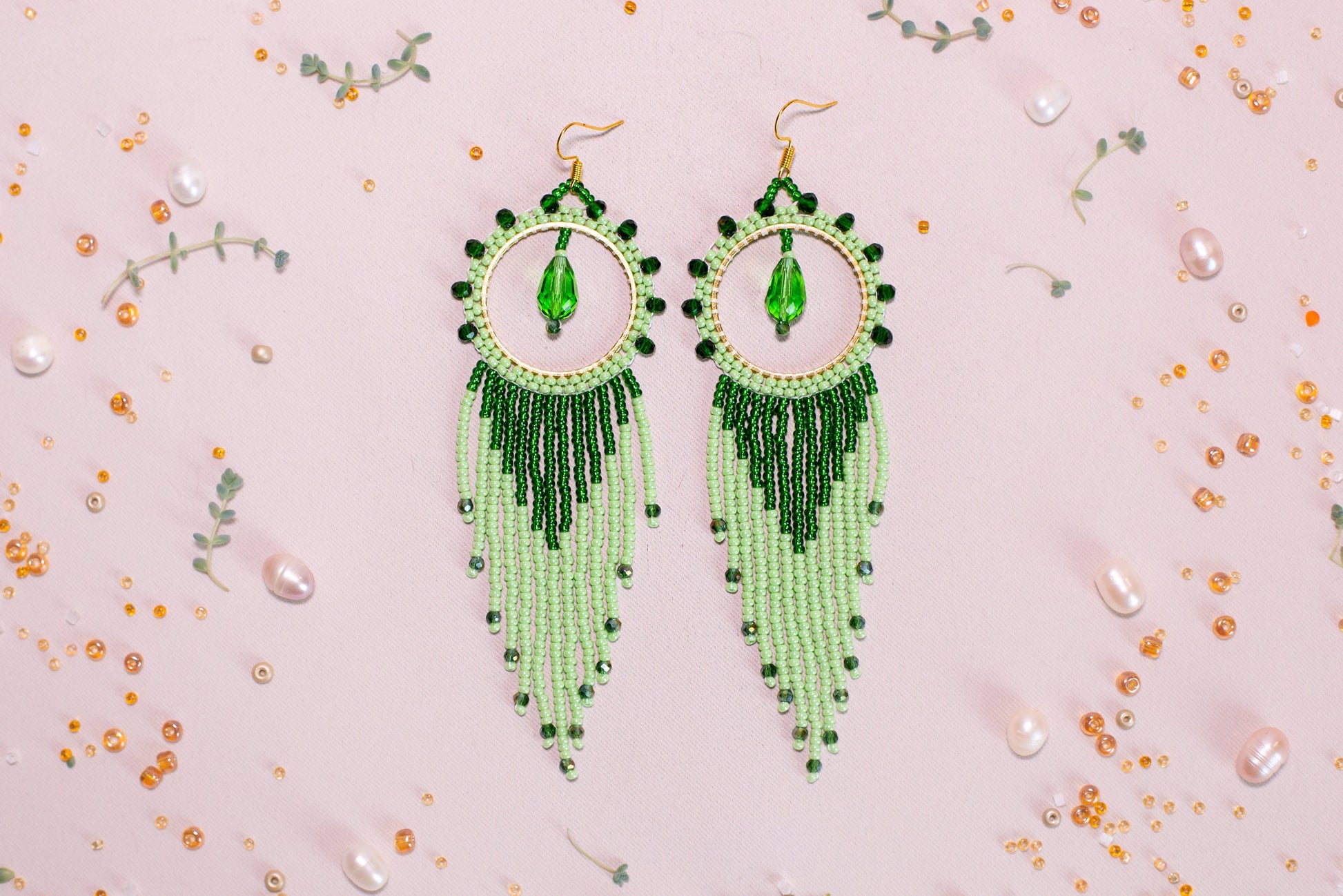 a pair of green beaded earrings on a pink background