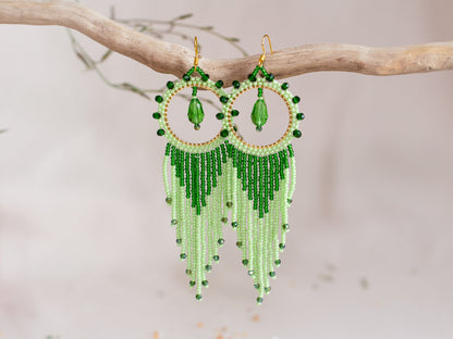 a pair of green beaded earrings hanging from a tree branch